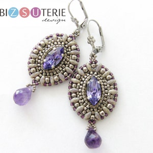 Puede incluir: Un par de pendientes de plata con una piedra preciosa púrpura en el centro de cada pendiente. Los pendientes están rodeados de pequeñas cuentas blancas y plateadas. Cada pendiente tiene una gota de amatista púrpura que cuelga de la parte inferior.