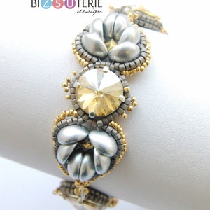 Pode incluir: Um bracelete de contas prateadas e douradas com uma grande peça central de cristal. O bracelete apresenta um design floral com múltiplas camadas de contas.