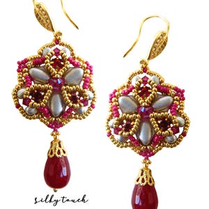 May include: A pair of gold earrings with a pink and silver beaded flower design and a dangling red gemstone. The earrings are labeled "silky touch beading pattern by b'zSuterie design".