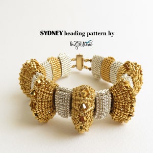 May include: A gold and silver beaded bracelet with a clasp closure. The bracelet features a repeating pattern of small beads and larger beads with a pointed design. The text "SYDNEY beading pattern by bizSutterie" is visible above the bracelet.