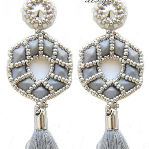 May include: A pair of silver earrings with a gray geometric design and a gray tassel. The earrings feature a clear crystal in the center.