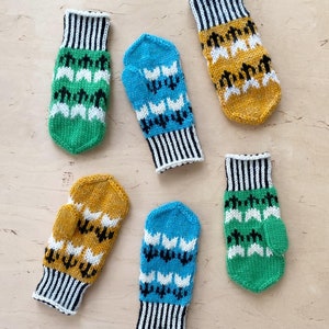 May include: Six pairs of knitted mittens in various colours and patterns. The mittens are green, blue, and yellow with white and black accents. The mittens are arranged in a grid pattern on a light wood surface.