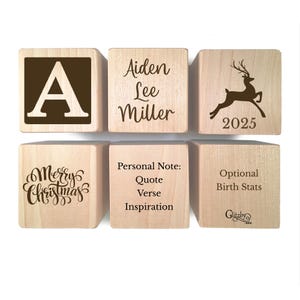May include: Six light-colored wooden blocks arranged in two rows. The blocks feature dark brown engravings including the letter A, the name Aiden Lee Miller, a leaping deer with the year 2025, the text Merry Christmas, Personal Note, and Birth Stats.