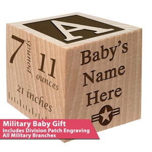 May include: A wooden block with a brown letter A on one side, and the text "Baby's Name Here" on another side. The block also has a ruler on one side, showing 21 inches, 7 pounds, and 11 ounces. The block has a brown star with two brown stripes on the bottom side. The text "Military Baby Gift Includes Division Patch Engraving All Military Branches" is below the block.