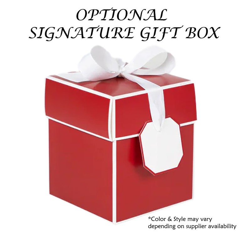 May include: A square red gift box with white trim, topped with a white ribbon bow and a blank white gift tag. The text OPTIONAL SIGNATURE GIFT BOX appears above the box, and the text *Color & Style may vary depending on supplier availability appears below.