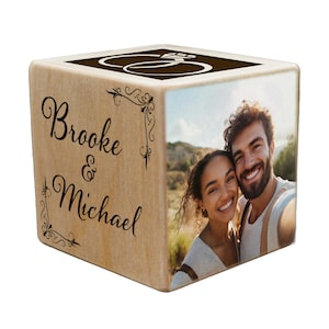 May include: A wooden cube with a photo of a couple on one side and the text "Brooke & Michael" on another side. The top of the cube has a decorative ring design.