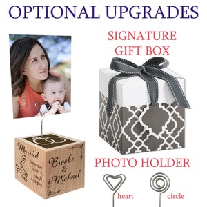 May include: A wooden photo holder with a heart and circle clip. The holder is engraved with the words "Married", "Saturday June 7, 2018 1:30 pm", "Brooke & Michael". The holder is displayed with a photo of a mother and child. A gray and white gift box with a gray ribbon is also shown.