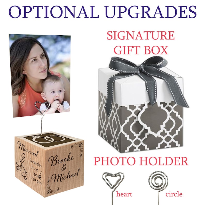 May include: A wooden photo holder with a heart and circle clip. The holder is engraved with the words "Married", "Saturday June 7, 2018 1:30 pm", "Brooke & Michael". The holder is displayed with a photo of a mother and child. A gray and white gift box with a gray ribbon is also shown.