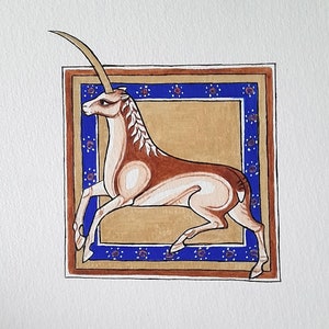 Könnte beinhalten: Eine handgemalte Illustration eines Oryx, einer Antilopenart, in einem dekorativen Rahmen. Der Oryx ist braun und weiß mit einem langen, gebogenen Horn. Der Rahmen ist blau, gold und rot mit einem sich wiederholenden Blumenmuster.