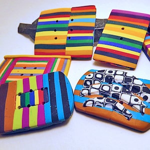May include: Assortment of colorful striped and patterned polymer clay buttons. The buttons are rectangular and oval shaped with various colors including red, orange, yellow, green, blue, purple, black, and white.