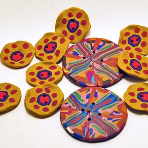 May include: A collection of handmade buttons including two large circular buttons with a multicoloured marbled pattern and several smaller mustard yellow buttons featuring a central purple hexagon and a ring of six red dots around the centre.