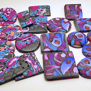 Puede incluir: Surtido de botones de arcilla polimérica hechos a mano, coloridos y con diseños abstractos en tonos de rosa, azul, morado y gris. Los botones son de varias formas y tamaños, incluyendo redondos, cuadrados y rectangulares.