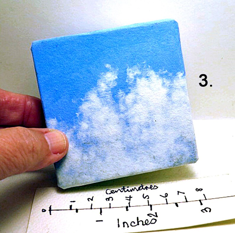 May include: A small, square canvas painting depicting a blue sky with white clouds. The canvas is approximately 3 inches by 3 inches.