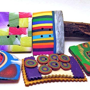 Può includere: Cinque bottoni quadrati e rettangolari con vari motivi e colori. Un bottone ha una griglia multicolore, un altro ha strisce orizzontali, uno è blu con un disegno circolare, uno è viola con piccoli cerchi e uno è verde e rosso.