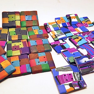 Könnte beinhalten: Eine Sammlung quadratischer Knöpfe mit mehrfarbigen geometrischen Mustern. Die Knöpfe sind in zwei Gruppen angeordnet, wobei einige ein gitterartiges Design aufweisen und andere abstrakte, marmorierte Farbblöcke in verschiedenen Tönen zeigen.