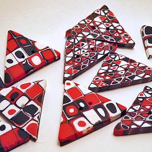 May include: A collection of nine triangular polymer clay buttons with a geometric pattern in red, black, and white.