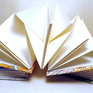 May include: A handmade book with white pages bound with a colorful map design. The pages are fanned out to show the binding.
