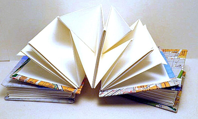 May include: A handmade book with white pages bound with a colorful map design. The pages are fanned out to show the binding.