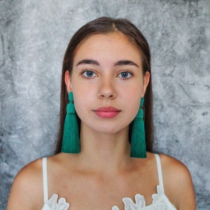Peut inclure: Une femme portant un haut en dentelle blanche avec de longues boucles d'oreilles à franges vertes.