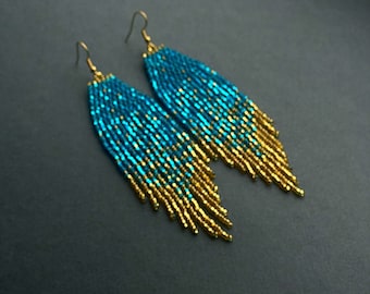 May include: A pair of long, beaded earrings with a gradient of turquoise and gold beads. The earrings are dangle style and have a simple hook closure.