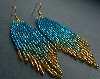 May include: A pair of long, beaded earrings with a gradient of blue and gold beads. The earrings are made with small, round beads that are strung together in a cascading pattern.