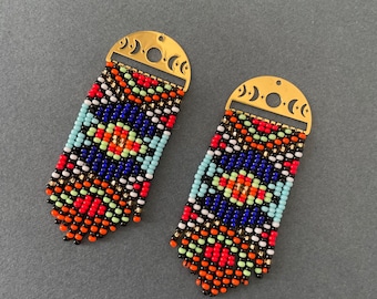 Pode incluir: Um par de brincos de contas com um padrão geométrico em tons de vermelho, laranja, amarelo, azul, preto e branco. Os brincos são presos a argolas de metal dourado com um design de lua crescente.