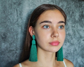May include: A woman wearing a pair of long, green tassel earrings. The earrings are made of beads and have a teardrop shape.