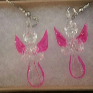 Puede incluir: Un par de pendientes de &aacute;ngel de vidrio transparente con alas rosas. Los pendientes cuelgan de ganchos plateados.