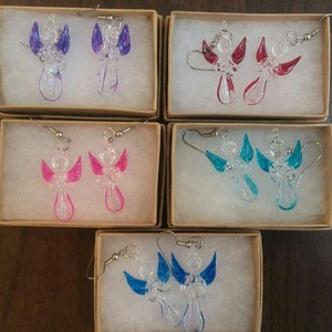 Puede incluir: Cinco peque&ntilde;as cajas, cada una con un par de pendientes de cristal en forma de &aacute;ngel. Los pendientes son de varios colores, incluyendo morado, rosa, rojo, azul y turquesa.