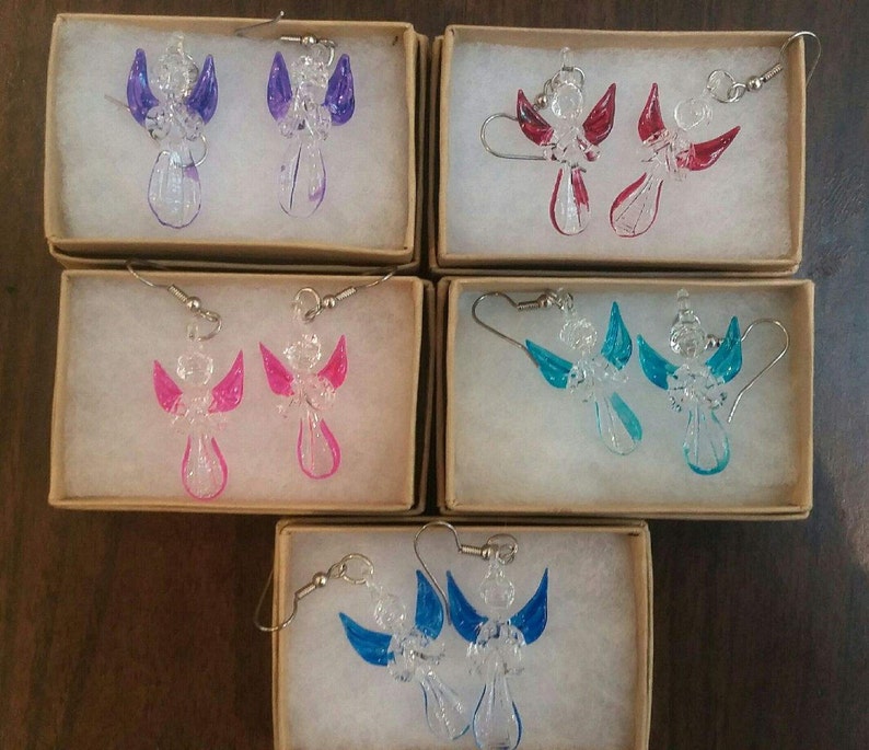 Puede incluir: Cinco peque&ntilde;as cajas, cada una con un par de pendientes de cristal en forma de &aacute;ngel. Los pendientes son de varios colores, incluyendo morado, rosa, rojo, azul y turquesa.