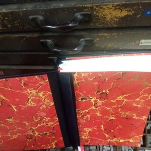 K&ouml;nnte beinhalten: Zwei rote und gold marmorierte Hardcover-B&uuml;cher mit schwarzen R&uuml;ckseiten und wei&szlig;en Band-Lesezeichen. Die B&uuml;cher liegen auf einer Oberfl&auml;che mit einem Raster aus Metalltypen.