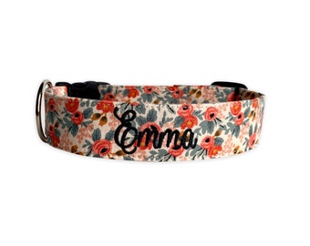 May include: A pet collar featuring a floral pattern with coral-colored roses and sage green leaves on a cream background. The name Emma is embroidered in black script lettering on the front. It includes a black plastic buckle and a metal D-ring.