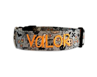 May include: A gray pet collar featuring a Halloween-themed pattern of candy corn, pumpkins, ghosts, bats, and spiderwebs. The name VALOR is embroidered in bright orange thread across the center of the collar, which includes a black buckle.