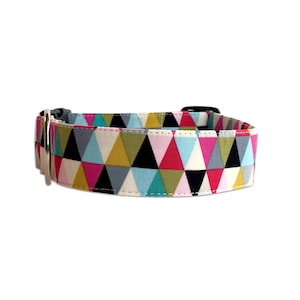 May include: A colourful dog collar with a geometric pattern of triangles in shades of pink, blue, green, yellow, black and grey. The collar has a silver buckle and is made of fabric.