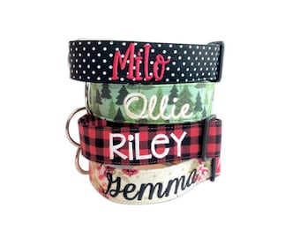May include: A stack of four pet collars featuring different patterns and embroidered names. The top collar is black with white polka dots and the name Milo in red. The second is green with a tree print and the name Ollie in white. The third is red and black plaid with the name Riley in white. The bottom collar has a floral pattern and the name Gemma in black.