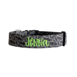 May include: Gray dog collar with a black bat pattern and the name "Jenna" embroidered in bright green. The collar has a black plastic buckle and a metal D-ring for leash attachment. A festive accessory for pets.