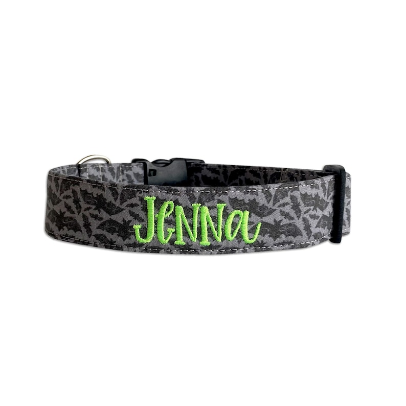 May include: Gray dog collar with a black bat pattern and the name "Jenna" embroidered in bright green. The collar has a black plastic buckle and a metal D-ring for leash attachment. A festive accessory for pets.