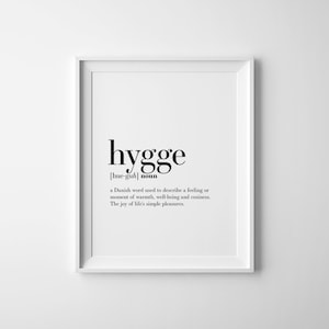 K&ouml;nnte beinhalten: Ein wei&szlig;er gerahmter Druck mit dem Wort "hygge" in Schwarz, darunter die Aussprache und das Wort "Nomen". Die Definition, die ein Gef&uuml;hl von W&auml;rme und Wohlbefinden beschreibt, ist in kleinerer Schrift gedruckt.