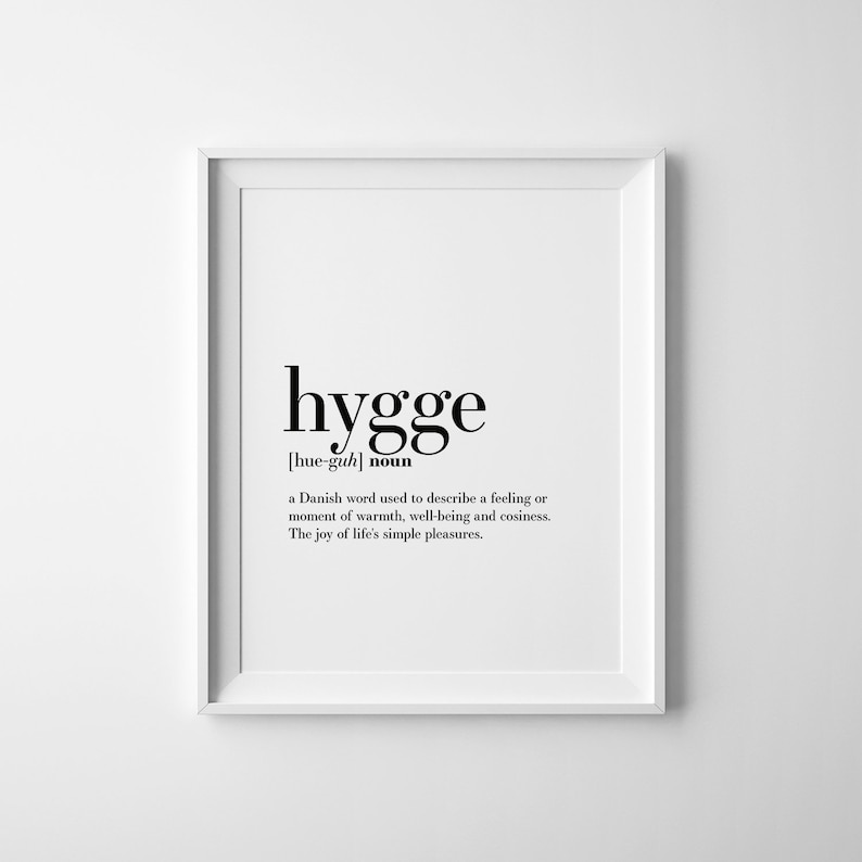 K&ouml;nnte beinhalten: Ein wei&szlig;er gerahmter Druck mit dem Wort "hygge" in Schwarz, darunter die Aussprache und das Wort "Nomen". Die Definition, die ein Gef&uuml;hl von W&auml;rme und Wohlbefinden beschreibt, ist in kleinerer Schrift gedruckt.