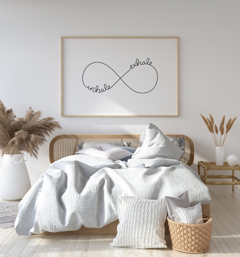 May include: A white bed with a light blue duvet and a white pillow. The bed has a wooden frame with a woven headboard. A framed print with the words "inhale exhale" in an infinity symbol is hanging on the wall behind the bed.