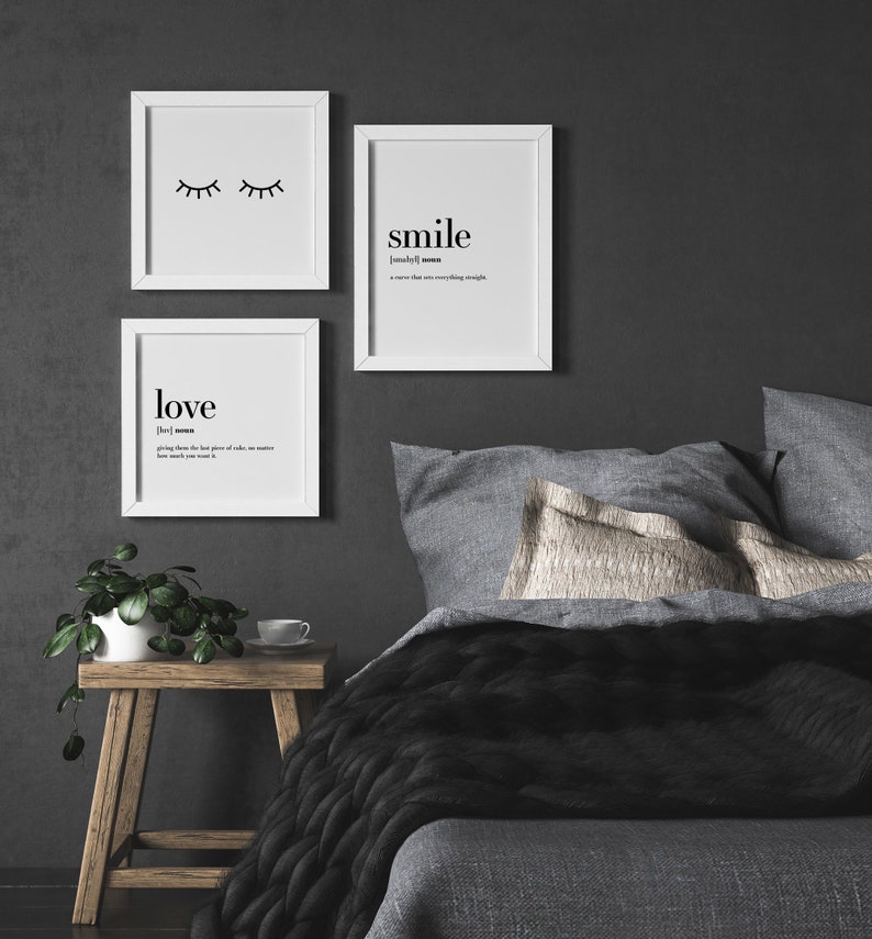 May include: Three framed prints with black text on a white background. The top print has a simple illustration of closed eyes. The middle print says "smile" and defines it as "a curve that sets everything straight." The bottom print says "love" and defines it as "giving away the last piece of cake, no matter how much you want it."