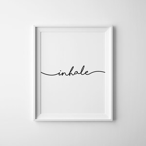 May include: A framed print with the word "inhale" in elegant black script. The word is centered on a white background, and the frame is white. The minimalist design is suitable for home decor.