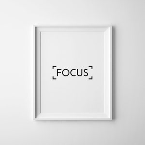 Puede incluir: Una impresi&oacute;n enmarcada en blanco con la palabra "FOCUS" en texto negro dentro de un corchete cuadrado negro.