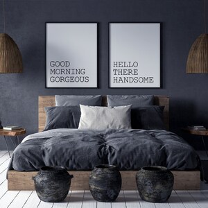 May include: A dark gray bedroom with a bed, two bedside tables, and two framed prints on the wall. The prints say "Good Morning Gorgeous" and "Hello There Handsome".