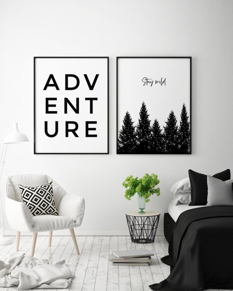 May include: Two black and white framed prints on a white wall. The print on the left says "ADVENTURE" in black text. The print on the right has a silhouette of a forest with the text "Stay wild" above it.