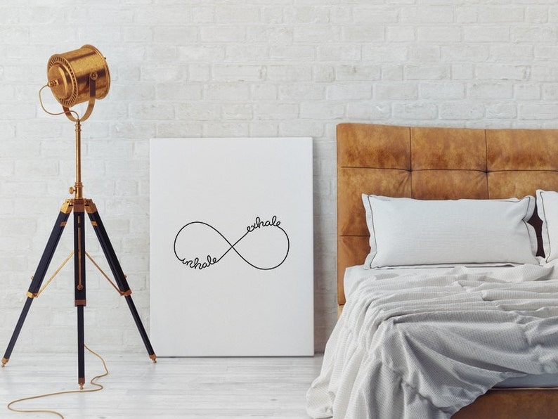 May include: A white canvas print featuring a black infinity symbol with the words "inhale" and "exhale" inscribed within it. The print is displayed against a white brick wall, above a brown leather headboard with white bedding.