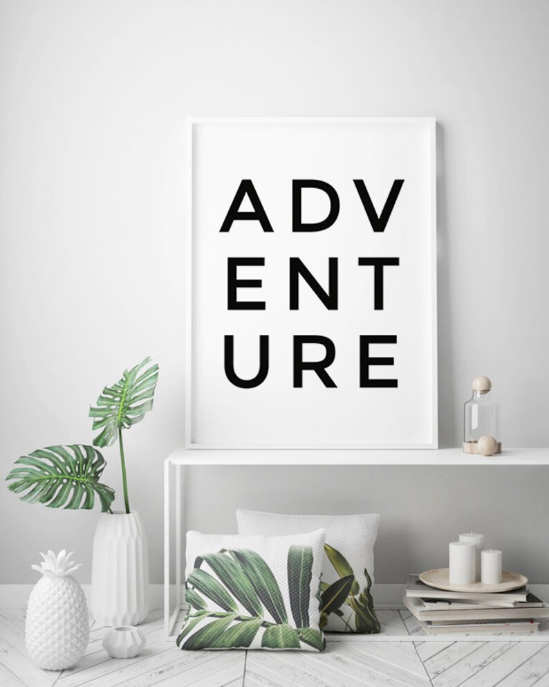 May include: A white framed print with the word "ADVENTURE" in black letters. The print is on a white shelf with a white vase with a green plant, a white pineapple, and a clear glass bottle with a wooden stopper.