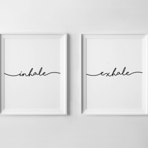May include: Two framed art prints with the words "inhale" and "exhale" in elegant black script. The minimalist design features a white background and a simple, flowing font, suitable for home decor.