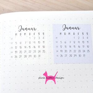 May include: Two square calendar stickers for the month of Januar on a dotted journal page. Each sticker features a black printed calendar grid with the days of the week labeled M, D, M, D, F, S, S and dates from 1 to 31. A pink cat logo with the text pink kitten design is below.