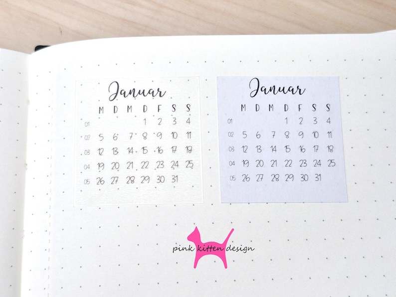 May include: Two square calendar stickers for the month of Januar on a dotted journal page. Each sticker features a black printed calendar grid with the days of the week labeled M, D, M, D, F, S, S and dates from 1 to 31. A pink cat logo with the text pink kitten design is below.